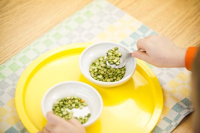 A picture of a young child scooping seeds from one bowl to another.